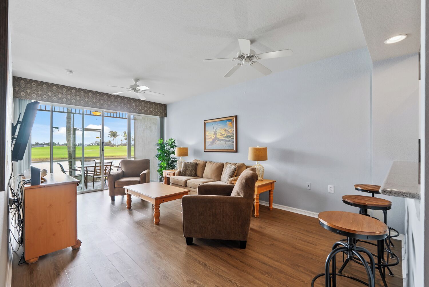 Un salon spacieux doté d’une grande fenêtre, d’un ventilateur de plafond, d’un ensemble de canapés, d’une table basse et d’un petit coin bar.