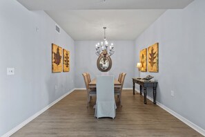 A dining room with a wooden table, chairs, a chandelier, and artwork on the walls.