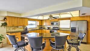A modern kitchen with wooden cabinets, a central island with chairs, stainless steel appliances, and a view of the outdoors. - Canal Grande Waterfront 6 Bedroom Holiday Home by Naples Florida (Naples)