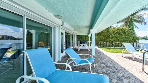 A covered outdoor area with lounge chairs, a barbecue grill, and a view of the water.