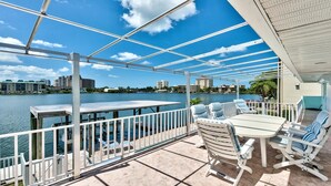 A covered outdoor area with a table and chairs, overlooking a body of water with buildings in the background. - Canal Grande Waterfront 6 Bedroom Holiday Home by Naples Florida (Naples)