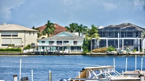 A waterfront property with a dock, a house with a balcony, and a large building with a glass facade. - Canal Grande Waterfront 6 Bedroom Holiday Home by Naples Florida (Naples)