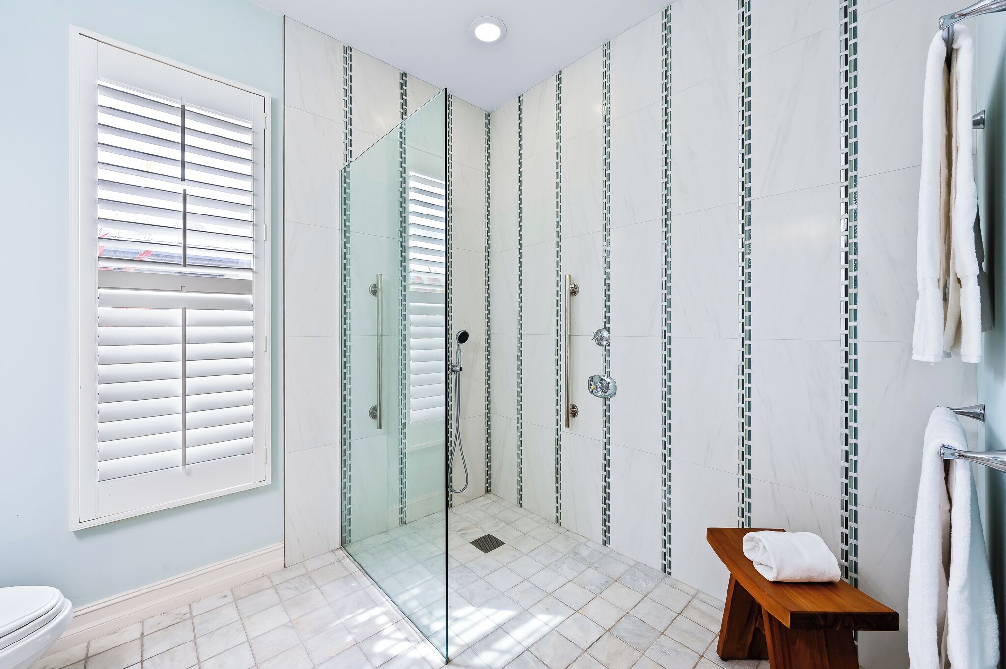 A modern bathroom with a glass-enclosed shower, white tiled walls, and a wooden bench.