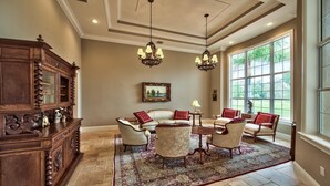 A spacious living room with a large window, a chandelier, and a wooden cabinet.