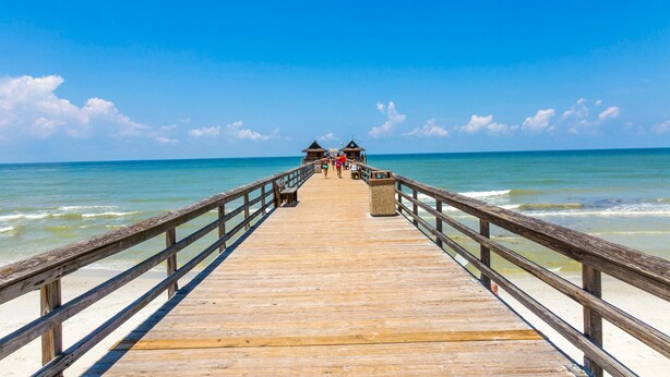 A wooden pier extending into the ocean with a clear sky.