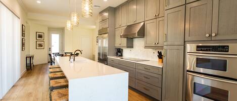 A modern kitchen with a large island, stainless steel appliances, and wooden flooring.