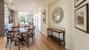 Een moderne keuken met houten kastjes, een eethoek met een houten tafel en stoelen, en een hal met kunstwerken in lijsten en een spiegel.