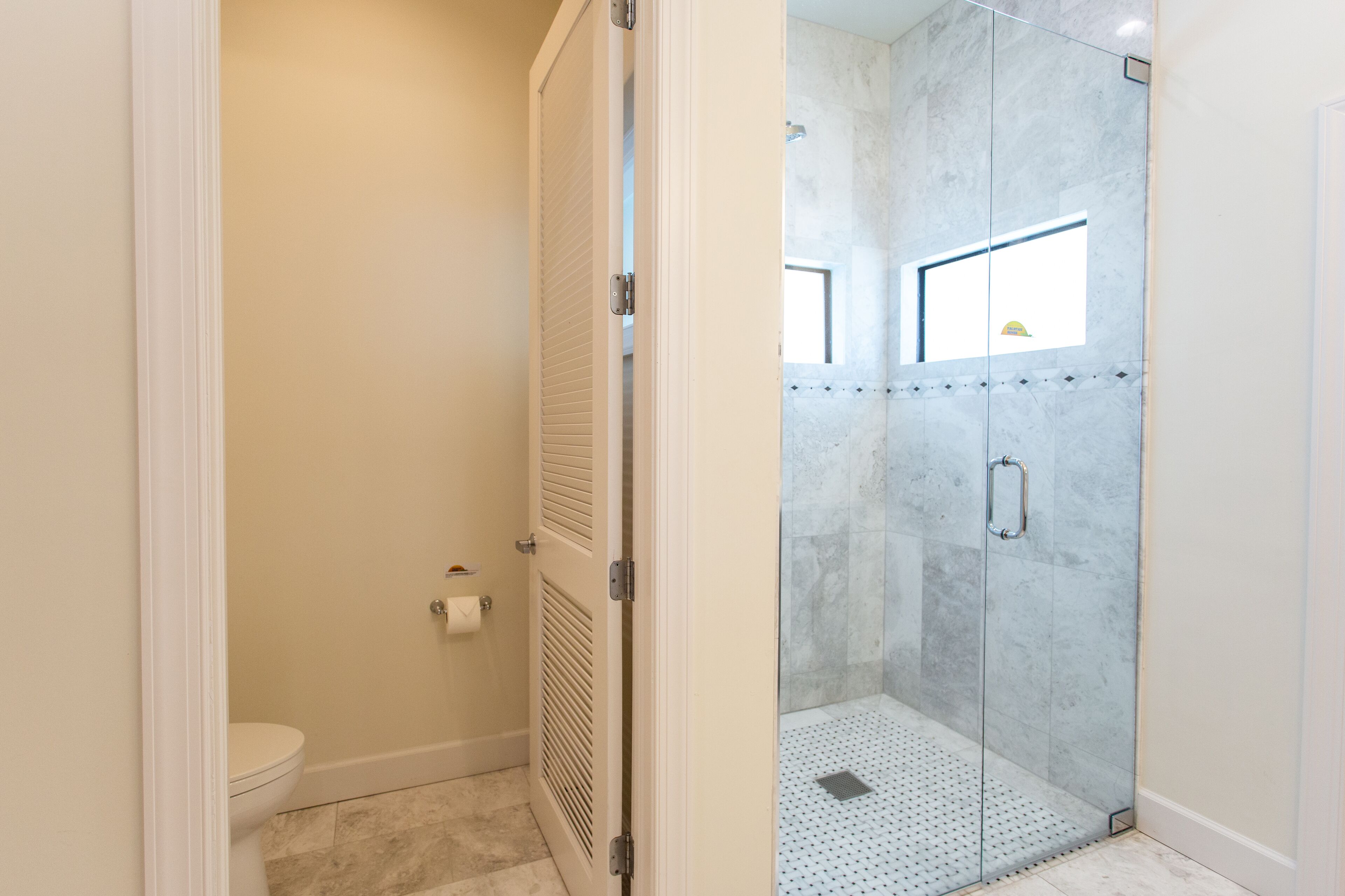 A bathroom with a toilet, a shower with a glass door, and a small window.