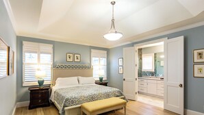 A bedroom with a bed, bedside tables, a bench, a ceiling light, and a door leading to a bathroom. - Tuscan Vacation Rental. Stylish 3-Bedroom Getaway Near Vanderbilt Beach Enjoy a Private Pool, Spacious Layout, and Modern Comforts Perfect for Families, Groups, and Pet-Friendly Stays (Naples)