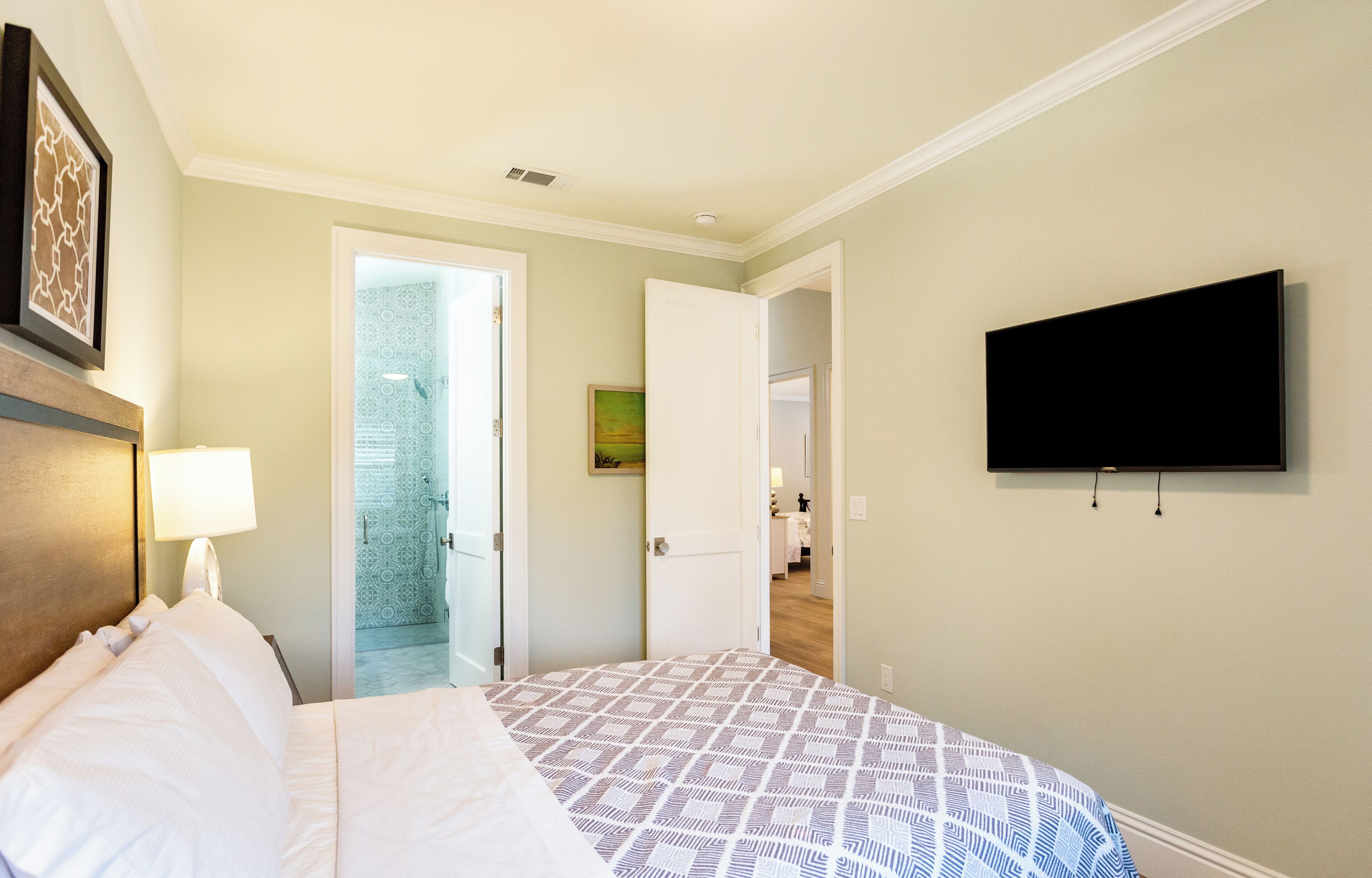 A hotel room with a bed, a TV mounted on the wall, and a bathroom visible through an open door.
