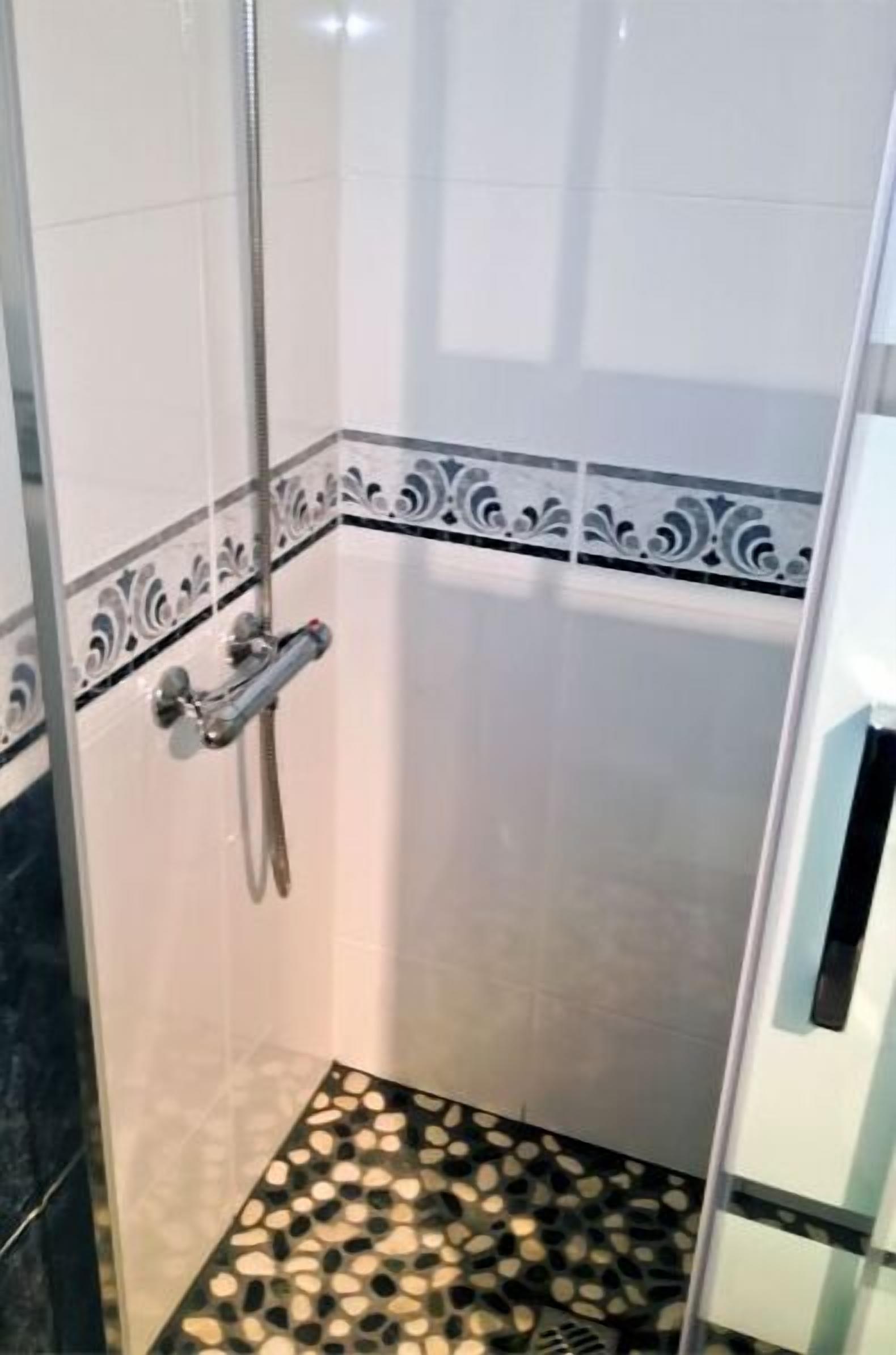 A shower with a glass door, a tiled floor with a black and white pattern, and a decorative border on the wall.