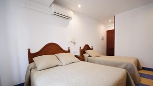 Una habitación de hotel con dos camas, una mesita de noche, un equipo de aire acondicionado y una puerta.