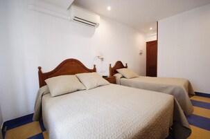 Una habitación de hotel con dos camas, una mesita de noche, un equipo de aire acondicionado y una puerta.