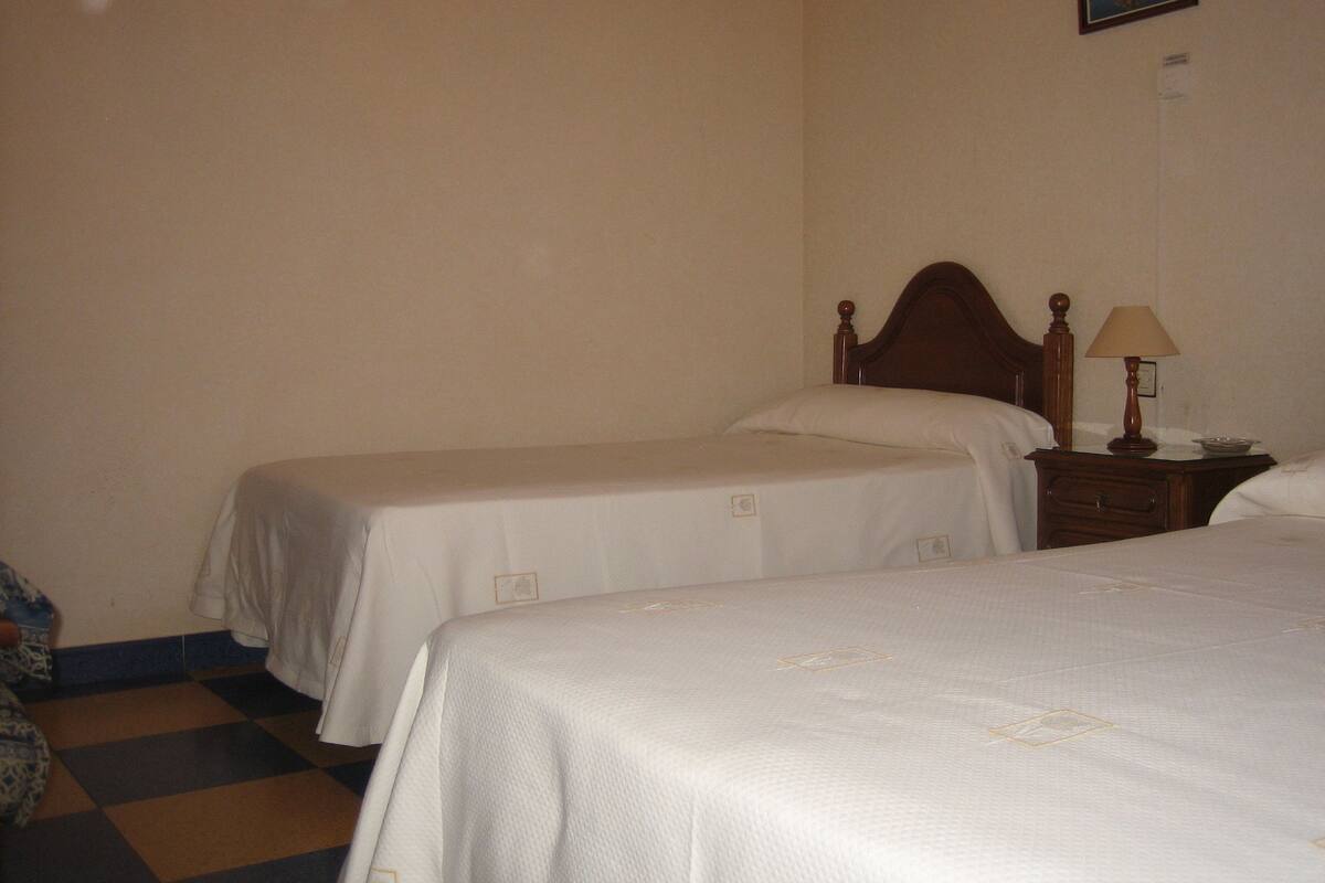 A hotel room with two single beds, a wooden nightstand with a lamp, and a checkered floor.