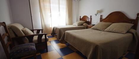 A hotel room with two beds, a chair, a nightstand, and a window with curtains.