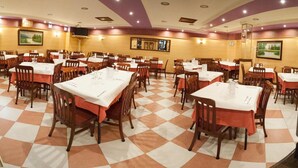 Un comedor con varias mesas y sillas, dispuesto sobre un piso con estampado de cuadros.