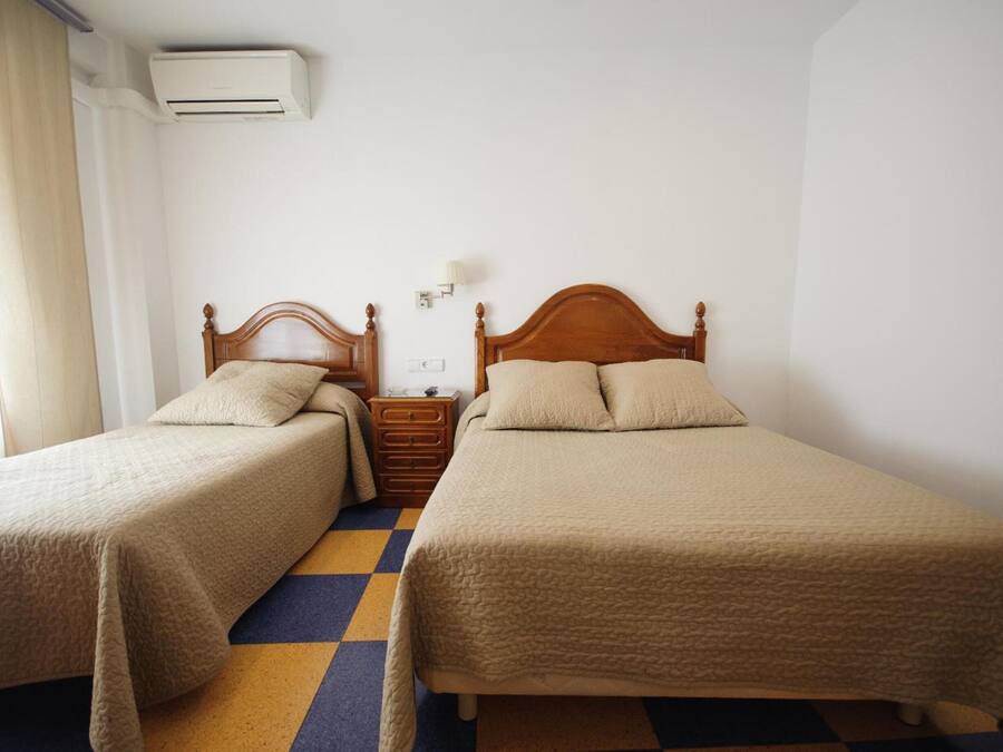 Una habitación con dos camas individuales, una mesita de noche, una lámpara y un equipo de aire acondicionado.