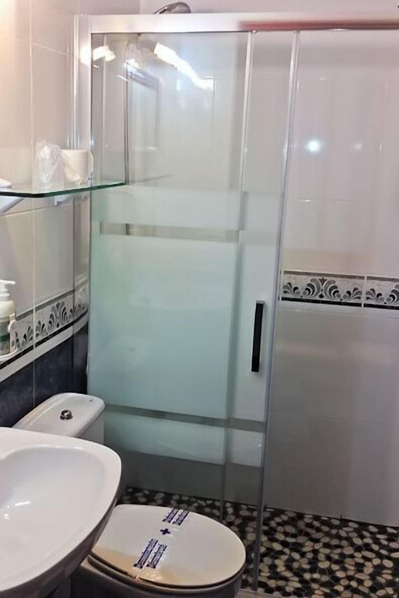 A bathroom with a glass-enclosed shower, a white sink, and a toilet.
