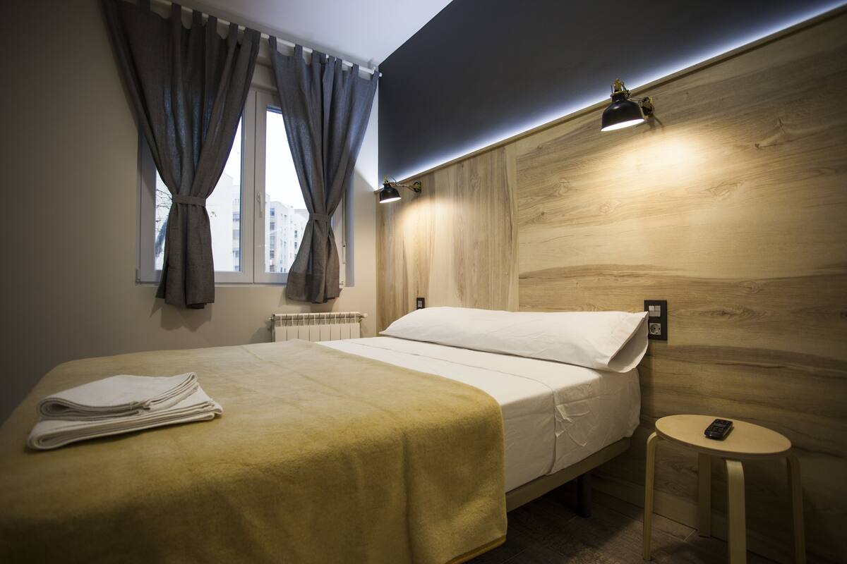 A hotel room with a bed, a small round table, a lamp, and a window with curtains.