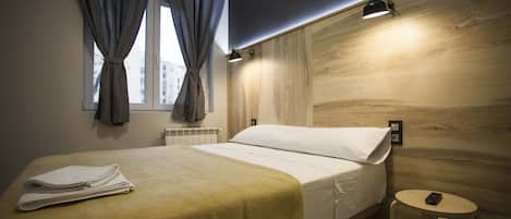 A hotel room with a bed, a small round table, a lamp, and a window with curtains.