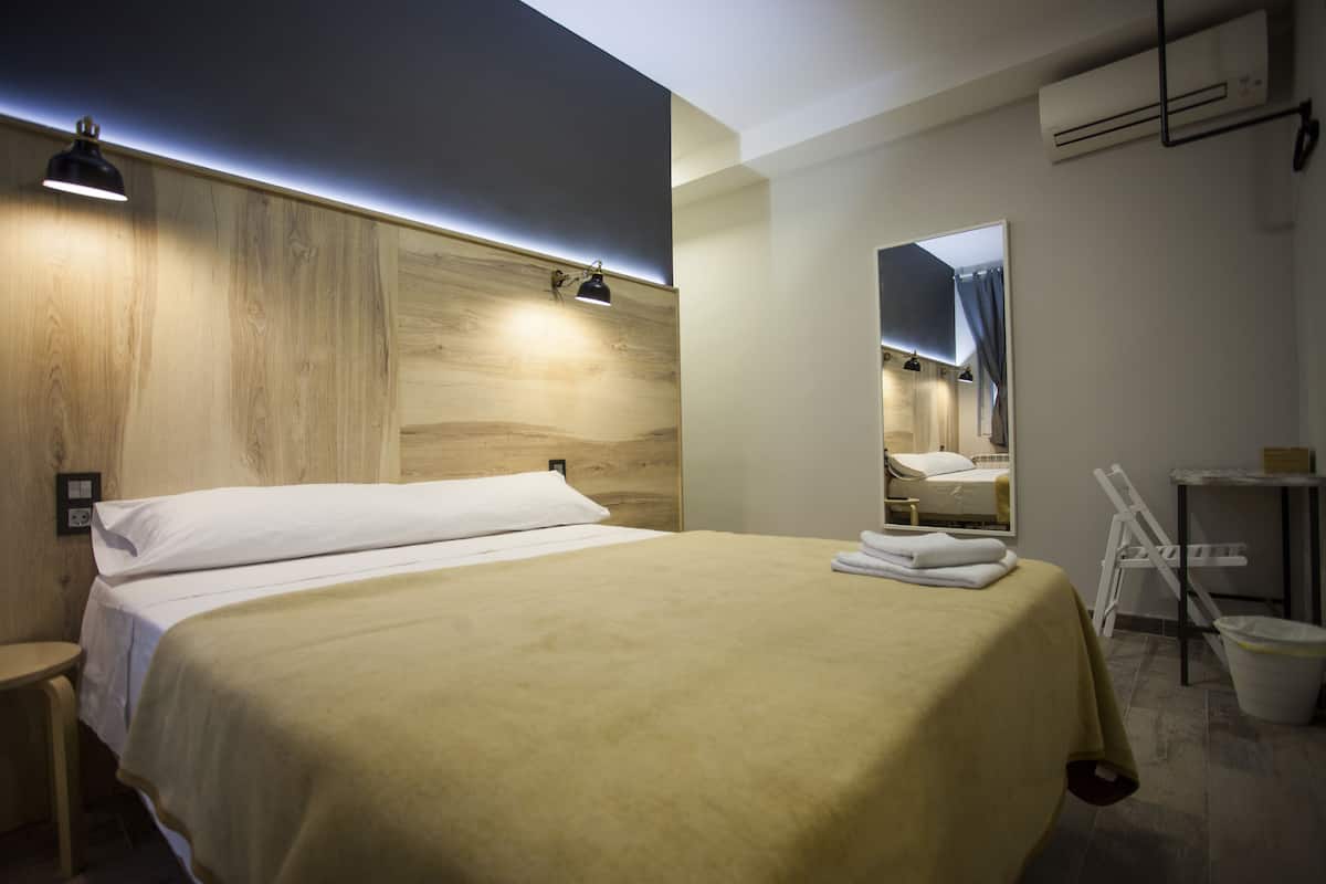 A modern hotel room with a large bed, bedside lamps, a mirror, a small table, and a chair.