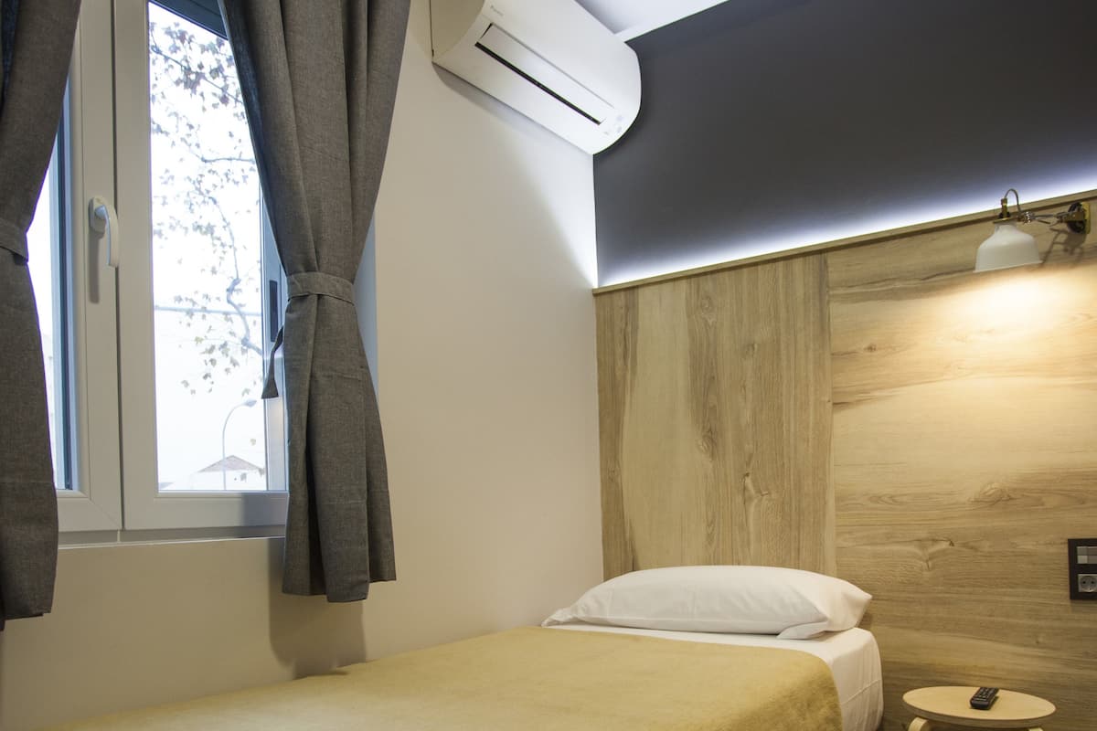 A small, neatly made bed with a yellow bedspread in a room with a wooden wall and a window with curtains.