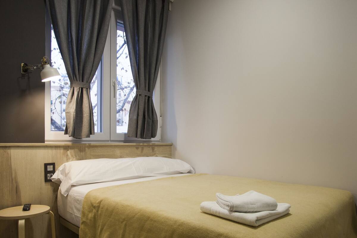 A bedroom with a bed, a bedside table, a lamp, and an air conditioning unit.
