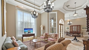 A spacious living room with a large TV, comfortable seating, and elegant chandeliers. - Knickerbocker Estate: Elegant 9-BR Getaway in Naples. Enjoy Private Pool, Outdoor Dining, and Expansive Grounds, Experience Tranquility with Easy Access to Naples' Best (Naples)