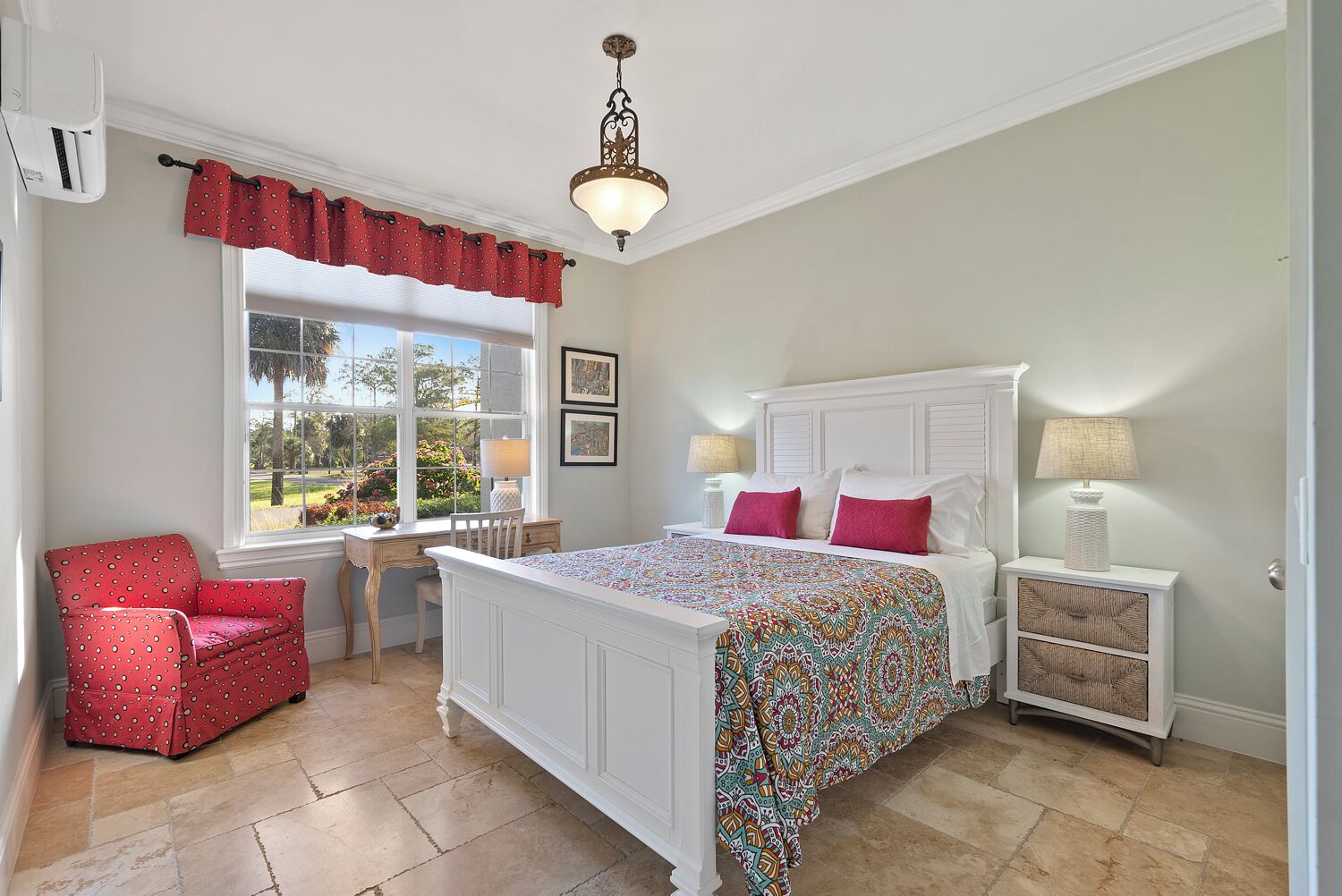 A bedroom with a large bed, a desk, a chair, a window with a view, and a chandelier.