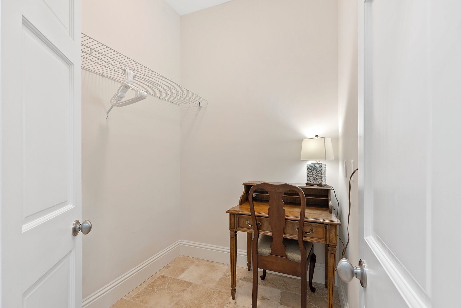 A small room with a wooden desk, a chair, a lamp, and a wire shelf.