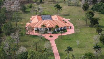 Stunning single-story house with a red-tiled roof, set amidst a lush lawn and mature trees.