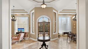 A spacious living area with a round table, a TV, and a dining area with chairs and a table. - Knickerbocker Estate: Elegant 9-BR Getaway in Naples. Enjoy Private Pool, Outdoor Dining, and Expansive Grounds, Experience Tranquility with Easy Access to Naples' Best (Naples)