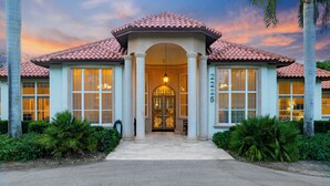 A two-story house with a tiled roof, large windows, and a central entrance with a glass door. - Knickerbocker Estate: Elegant 9-BR Getaway in Naples. Enjoy Private Pool, Outdoor Dining, and Expansive Grounds, Experience Tranquility with Easy Access to Naples' Best (Naples)