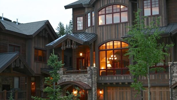 Une cabane en rondins à plusieurs étages, dotée d’une entrée en pierre, de grandes fenêtres et d’un balcon.