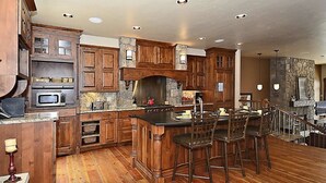 Une cuisine spacieuse avec des meubles en bois, un îlot central doté de tabourets, des appareils électroménagers intégrés et un mur d’accent en pierre.