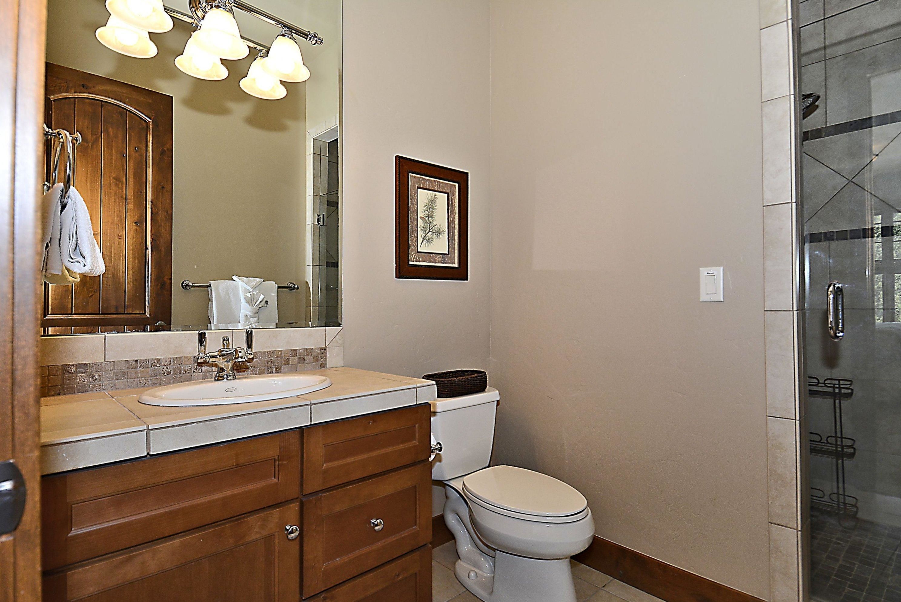 A bathroom with a wooden vanity, a sink, a toilet, a framed picture on the wall, and a glass shower enclosure.