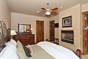 A bedroom with a bed, dresser, ceiling fan, fireplace, and framed picture on the wall. - Base Camp 480 4 Bedroom Holiday Home by Winter Park Lodging Company (Winter Park)