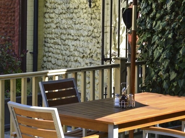 Una mesa de madera con un banco, una barandilla metálica y una pared de piedra al fondo.