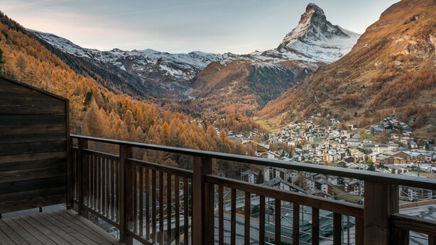 Een houten balkon met uitzicht op een vallei, een bergtop en een stad beneden.