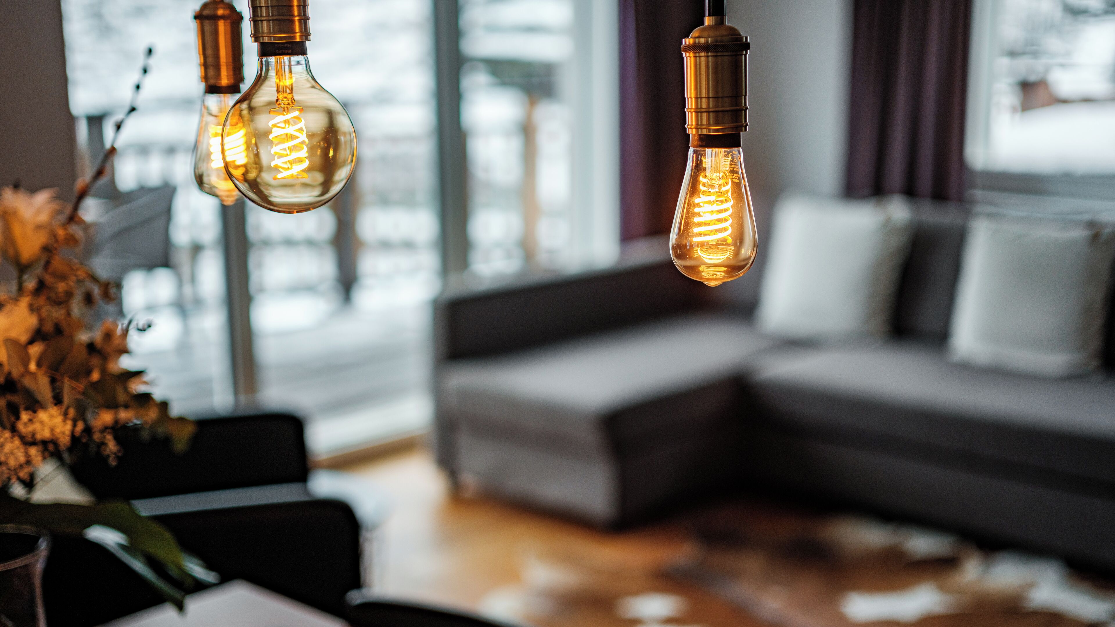 Ein modernes Wohnzimmer mit einer Eckcouch, einem Couchtisch und Edison-Glühbirnen, die von der Decke hängen.