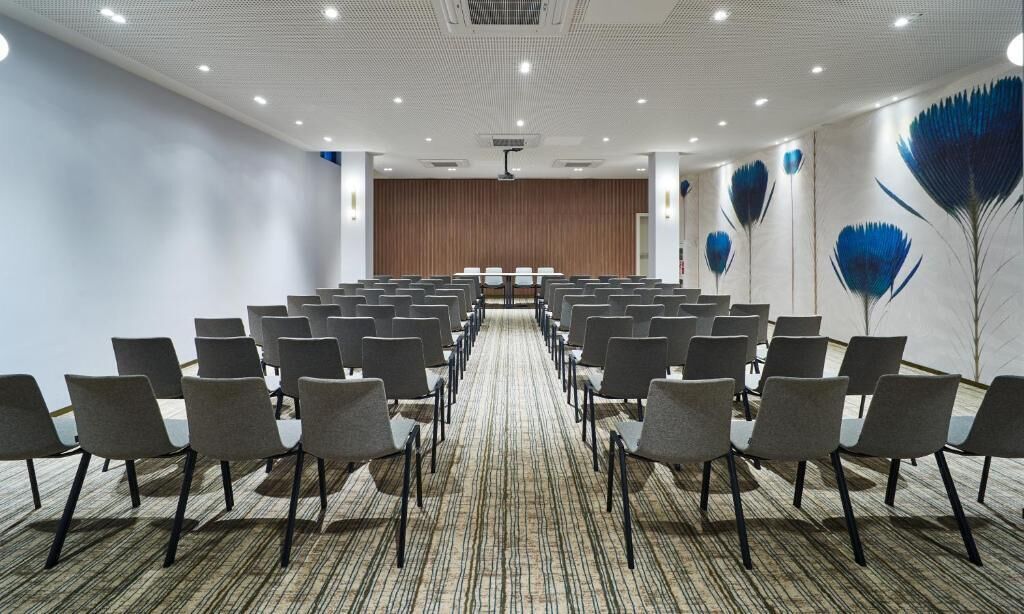 A conference room with rows of chairs, a carpeted floor, and a stage at the front.