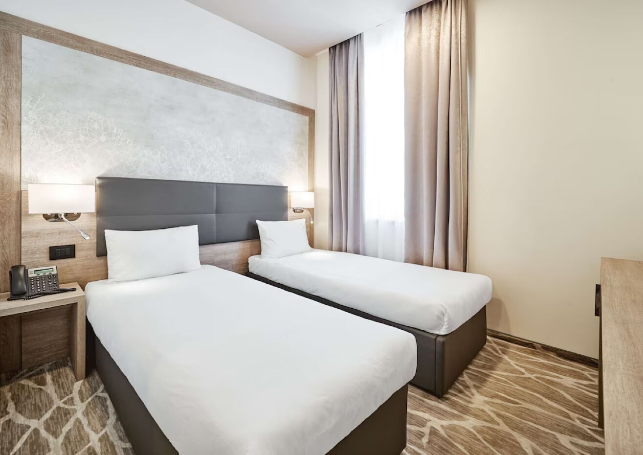 A hotel room with two beds, a desk with a phone, and a large abstract wall art piece.