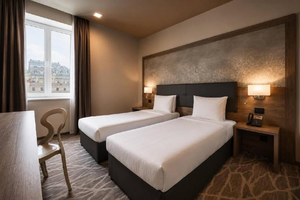 A hotel room with two beds, a desk, a chair, a window with curtains, and a city view.