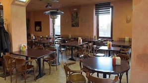 A restaurant with multiple tables and chairs, a ceiling fan, and a large window. - Hostal Sant Miquel (Balaguer)