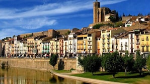A historic town with colorful buildings along a river, a prominent church tower, and a well-maintained waterfront. - Hostal Sant Miquel (Balaguer)