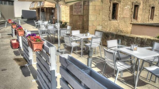 An outdoor café with tables and chairs, surrounded by stone walls and a building with windows. - Hostal Sant Miquel (Balaguer)