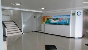 Un pasillo limpio y moderno con una escalera que conduce a un piso superior. Se observan obras de arte coloridas en las paredes, que representan escenas de la naturaleza.