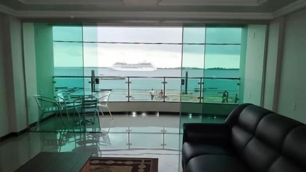 Una sala de estar con pared de vidrio que ofrece vista a un crucero y al mar.
