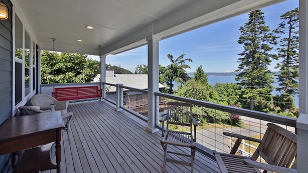 A covered deck with wooden furniture, a red bench, and a view of the ocean and trees. - The Lookout at Cranes Landing (Greenbank)