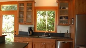 A kitchen with wooden cabinets, a stainless steel dishwasher, and a window with a view of greenery. - Goss Lake Chalet (Langley)